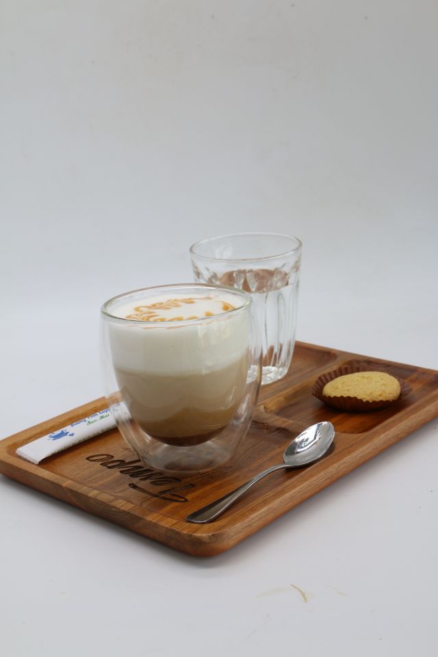 wooden tablet with a glas of latte macchiato, a glass of water, a spoon, a stick of sugar and a biscuit